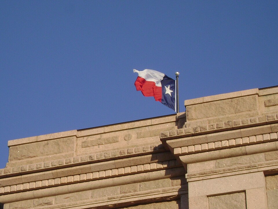 Texas state flag alongside gold and silver bullion coins representing tax-free precious metals buying